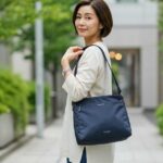 カナナショルダーバッグを持ち、自信を持って歩く40〜50代の日本人女性。都会的で落ち着いた雰囲気の街並み。